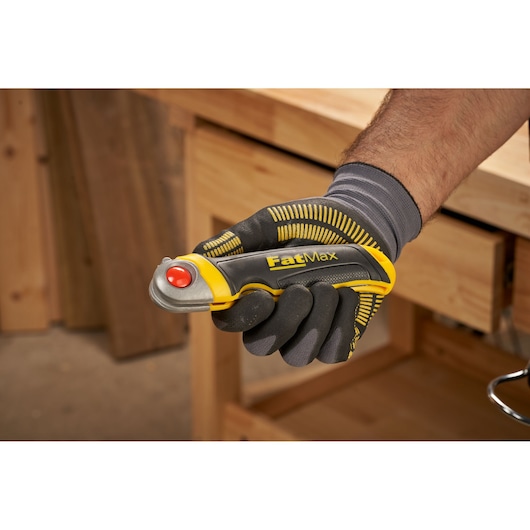 STANLEY FMHT0-20559 FatMax gereedschapsmes in een gehandschoende hand, gele en zwarte grip, werkplaats achtergrond.