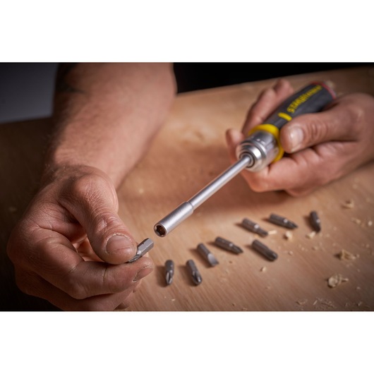 Photo du tournevis STANLEY FMHT0-62691 avec embouts interchangeables sur surface en bois, main insérant un embout.
