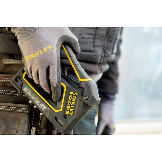 Agrafeuse STANLEY FMHT0-80550 tenue par une main gantée, gros plan, avec une ceinture à outils en arrière-plan.