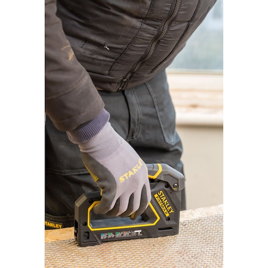 Photo de l'agrafeuse manuelle STANLEY FMHT0-80550 en utilisation, ouvrier avec gants fixant un treillis au bois.