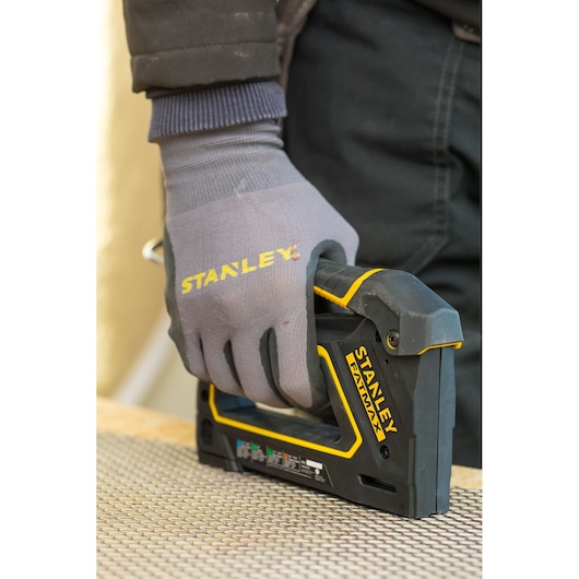 Agrafeuse STANLEY FMHT0-80550 en utilisation, tenue par une main gantée, outil noir et jaune sur une surface de travail.