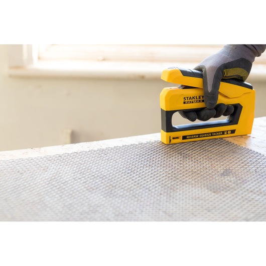 Stanley FMHT0-80551 tacker gebruikt op gaas, close-up hoek, geel-zwart ontwerp.