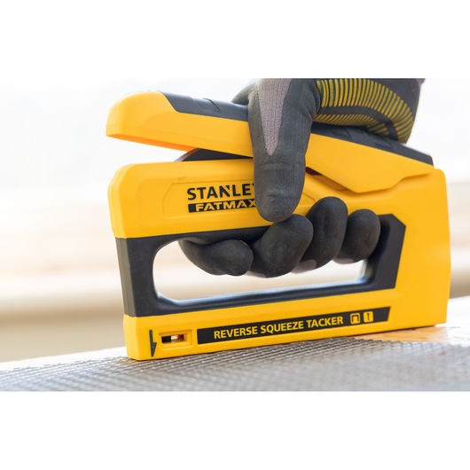 Foto van de STANLEY FMHT0-80551 tacker, geel en zwart, gebruikt met een gehandschoende hand op een oppervlak.
