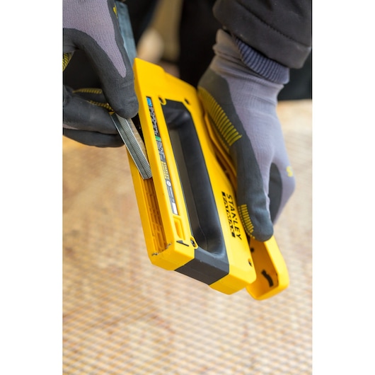 Foto van STANLEY FMHT0-80551 nietpistool dat wordt geladen, vastgehouden door gehandschoende handen, close-up.