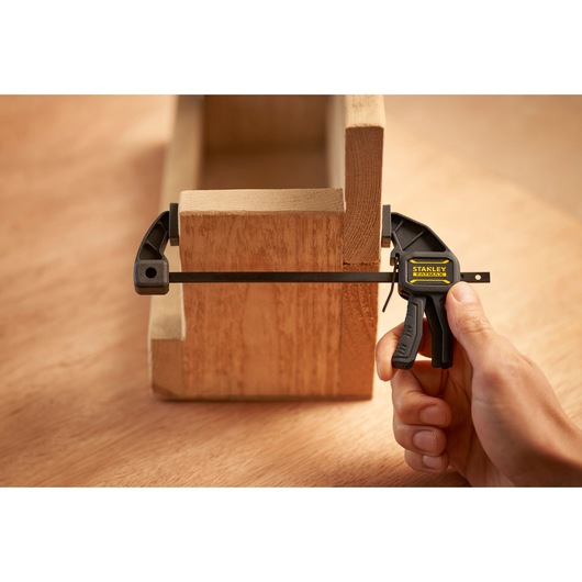 Photo du serre-joint rapide STANLEY FMHT0-83231 fixant deux pièces en bois, main utilisant le serre-joint en gros plan.