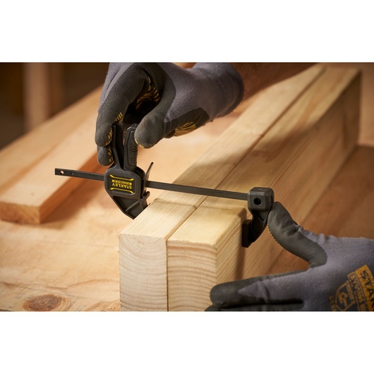Photo du serre-joint STANLEY FMHT0-83231 utilisé sur des blocs de bois par des mains gantées, vue rapprochée.