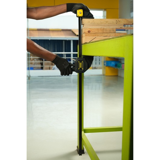 Serre-joint Stanley FMHT0-83241 utilisé pour fixer du bois sur un établi vert, vue latérale rapprochée.