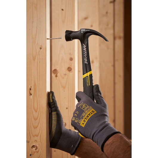 Foto van STANLEY FMHT1-51275 klauwhamer met zwart-gele handgreep die een spijker in houten balk slaat.