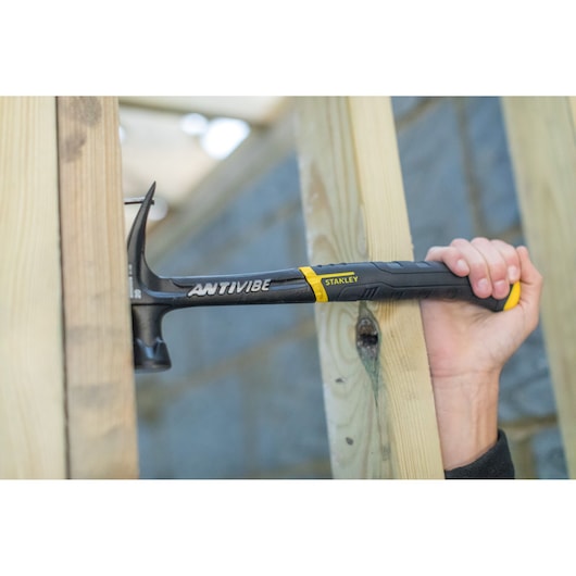 STANLEY FMHT1-51277 klauwhamer in gebruik, zwarte handgreep, slaat spijker in houten balken.