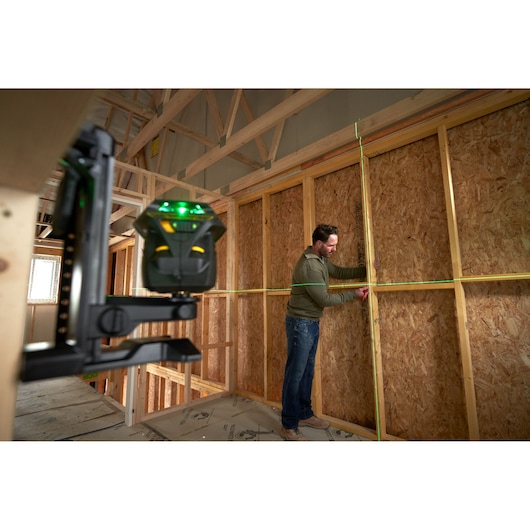 STANLEY FMHT1-77356 groene laserwaterpas projecteert horizontale en verticale lijnen in houten framekamer, werknemer markeert muur.