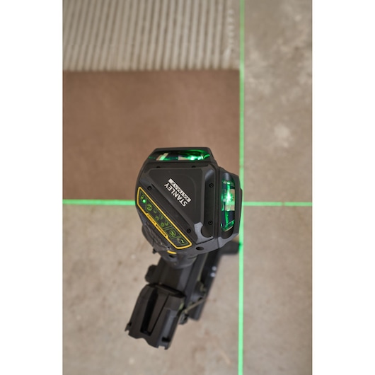 STANLEY FMHT1-77356 laserwaterpas die felle groene lijnen op een betegelde vloer projecteert, bovenaanzicht.