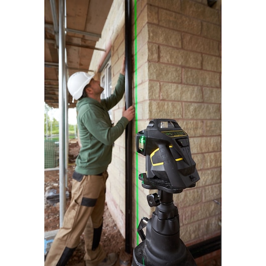 STANLEY FMHT1-77356 roterende laserwaterpas met groene lijn op muur, werknemer richt balk uit op bouwplaats.