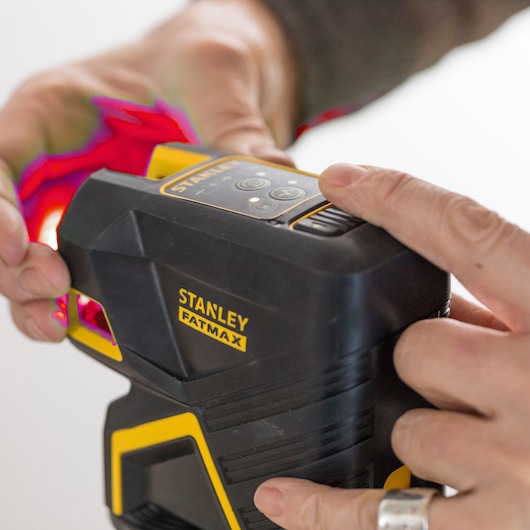 STANLEY SKU FMHT1-77414 FATMAX laserwaterpas, close-up fotografie, zwart en geel huis, handen bedienen.