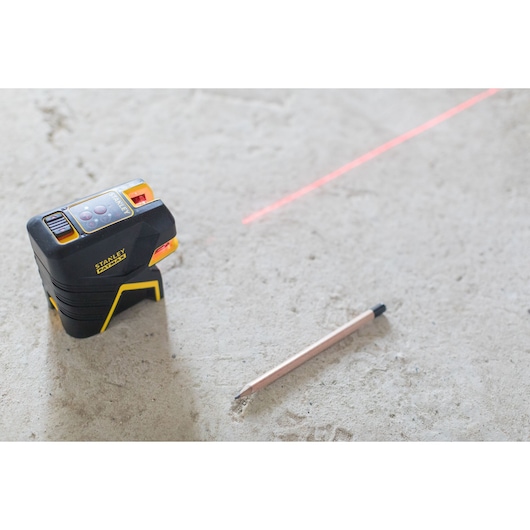 STANLEY FMHT1-77415 kruislijnlaser met zichtbare rode laserlijn en potlood op betonnen vloer, schuine aanzicht.