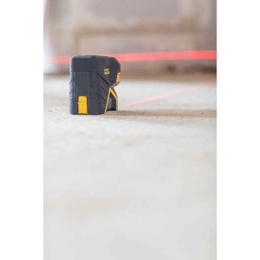 Stanley FMHT1-77415 kruislijnlaser op de vloer, zijaanzicht, met heldere rode laserlijnen.