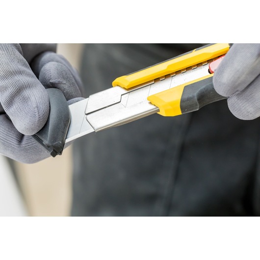 STANLEY FMHT10330-0 afbreekmes met gesegmenteerd lemmet en geel-zwarte handgreep, close-up tijdens gebruik.