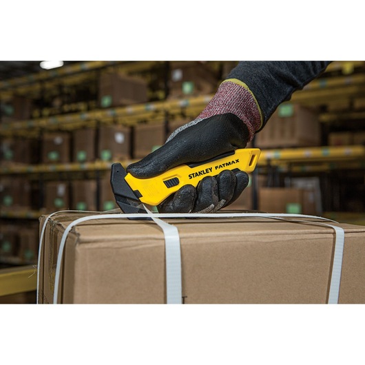 Stanley FMHT10358-0 stanleymes vastgehouden door een gehandschoende hand snijdt band van doos in magazijn.
