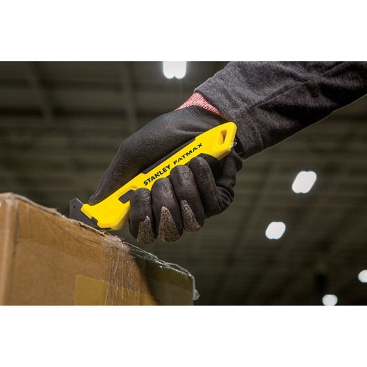 STANLEY FMHT10358-0 hobbymes met gele handgreep snijdt doos, vastgehouden in gehandschoende hand.
