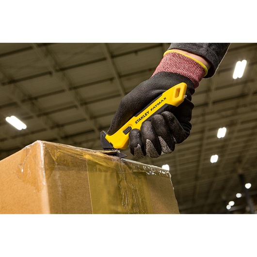 STANLEY FMHT10358-0 mes snijdt tape op kartonnen doos, werknemer draagt zwarte handschoenen.