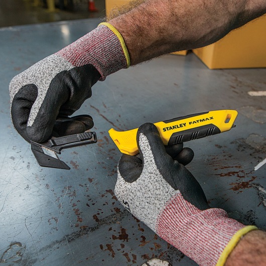 Foto van STANLEY FMHT10358 FATMAX stanleymes met gele handgreep, vastgehouden door gehandschoende handen.