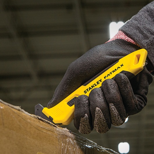 Stanley FMHT10358 hobbymes met gele handgreep, gebruikt voor het snijden van karton, vastgehouden door een gehandschoende hand.