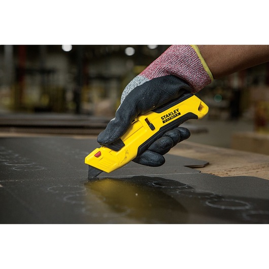Foto van STANLEY FMHT10365-0 hobbymes in gehandschoende hand die zwart materiaal snijdt in werkplaats.
