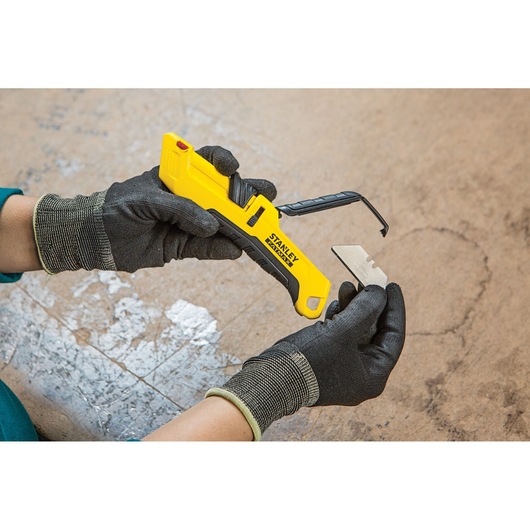 Foto van STANLEY FMHT10365-0 gereedschapsmes met gele handgreep en mes verwisseld door gehandschoende handen.