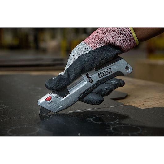 Foto van STANLEY FMHT10367-0 afbreekmes in gehandschoende hand die zwart materiaal snijdt.