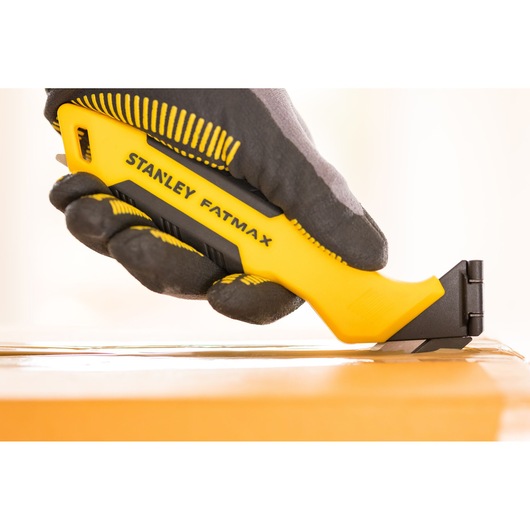 Foto van STANLEY FMHT10373-0 hobbymes in een handschoen, snijdt tape op een kartonnen doos.