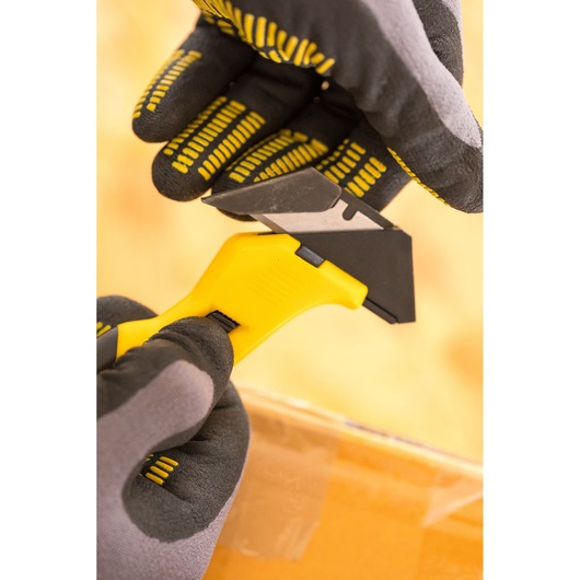 STANLEY FMHT10373-0 veiligheidsmes met gele handgreep, in gehandschoende handen die tape op een doos snijdt.