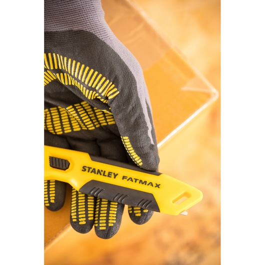 Foto van STANLEY FMHT10373-0 hobbymes vastgehouden door een gehandschoende hand, kartonnen doos op de achtergrond.