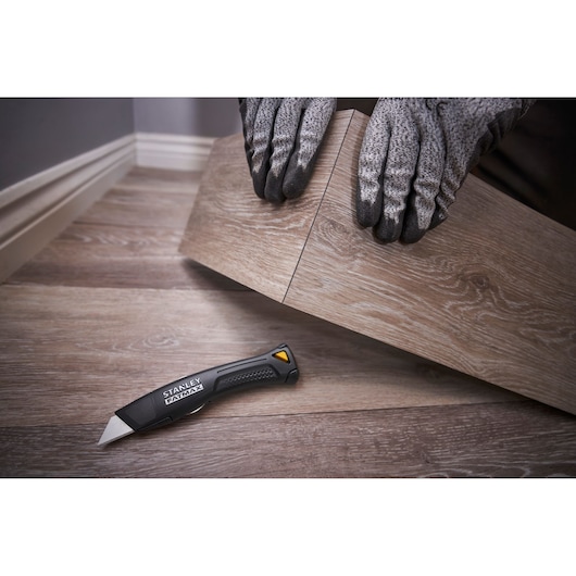 Cutter STANLEY FMHT10500-0 sur sol en bois, personne avec gants posant un sol en vinyle.