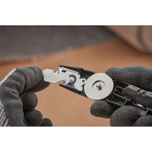 STANLEY FMHT10500-0 couteau utilitaire gros plan montrant changement de lame avec mains gantées.