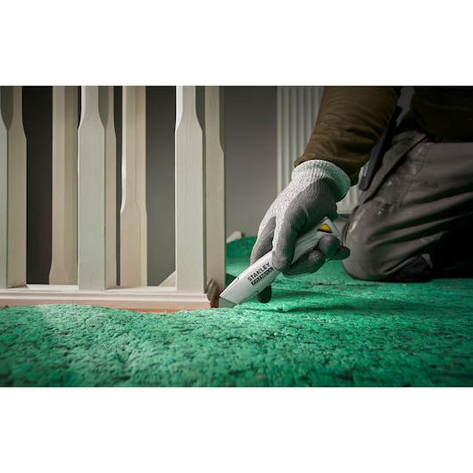 Stanley FMHT10501-0 couteau universel coupant un tapis vert près d'une rambarde blanche, photo en gros plan.