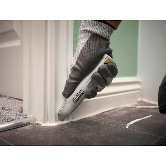 Couteau utilitaire STANLEY FMHT10501-0 utilisé pour couper du mastic le long d'une plinthe sur un sol carrelé.