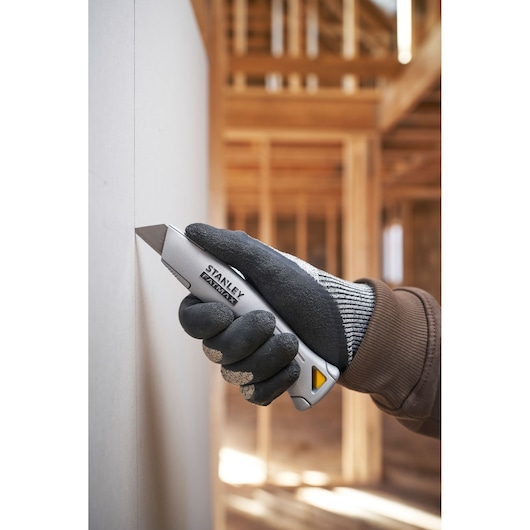 Photo du couteau utilitaire STANLEY FMHT10501-0 coupant du plâtre, tenu avec un gant sur un chantier.