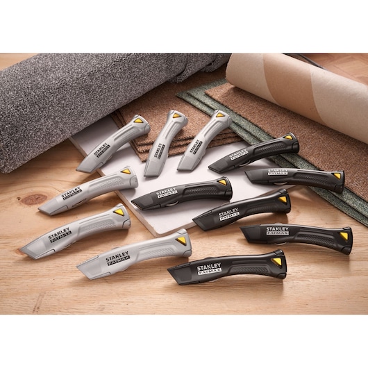 Couteaux utilitaires STANLEY FMHT10502-9 gris et noirs, posés sur une table en bois avec des rouleaux de tapis.