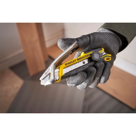 Photo du couteau utilitaire STANLEY FMHT10592-0 jaune et noir tenu dans une main gantée.
