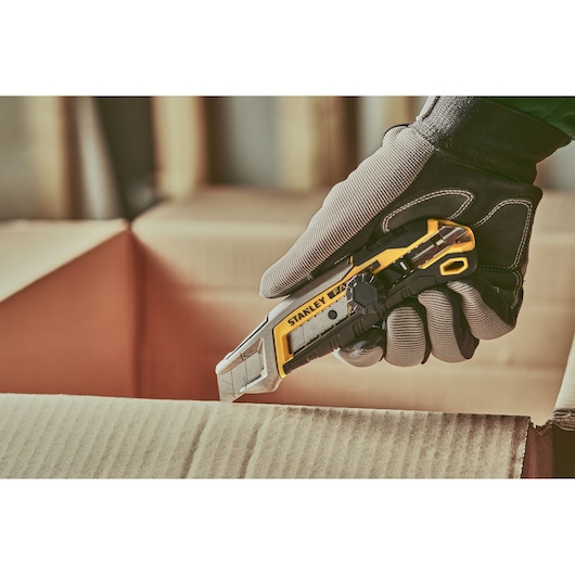 Stanley FMHT10592-0 couteau utilitaire coupant du carton, présenté dans une main gantée, photographie produit.