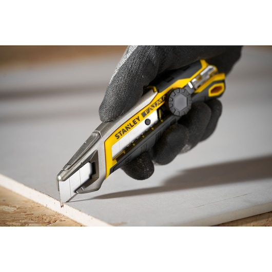 STANLEY FMHT10592-0 couteau utilitaire jaune et argent utilisé pour couper une plaque de construction.