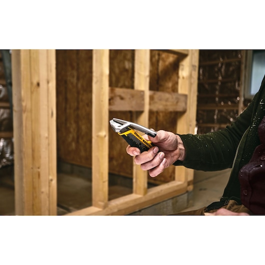 Couteau utilitaire STANLEY FMHT10592-0 tenu en main sur un chantier, poignée jaune et noire visible.