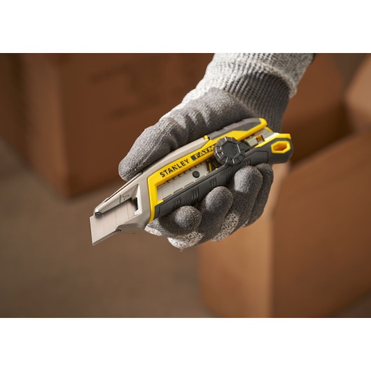 STANLEY FMHT10592-0 couteau utilitaire à manche jaune et gris tenu par une main gantée, photographie avec cartons.
