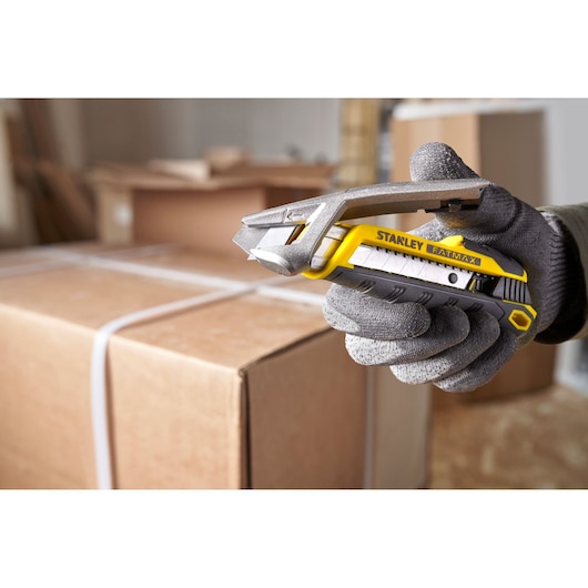Foto van STANLEY FMHT10594-0 FATMAX stanleymes in een gehandschoende hand boven een kartonnen doos.