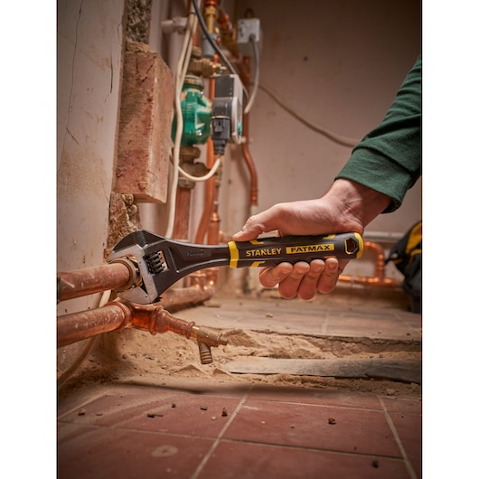 Foto van STANLEY FMHT13125-0 verstelbare sleutel gebruikt op koperen leidingen in een loodgietersomgeving.