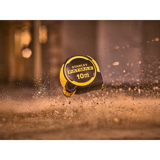 STANLEY FMHT33005-0 FATMAX 10m rolmaat geel en zwart, zwevend in een stoffige omgeving.
