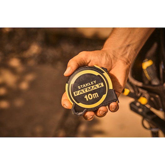 Foto van STANLEY FMHT33005-0 FatMax 10m rolmaat, zwart met gele behuizing, vastgehouden in een hand.