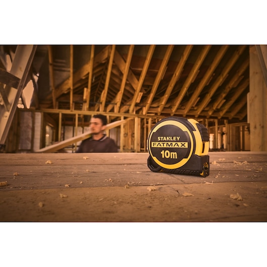 STANLEY FATMAX 10m rolmaat, SKU FMHT33005-0, op houten vloer bij bouwplaats.