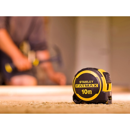 STANLEY FMHT33005-0 FatMax 10m meetlint geel en zwart, op werkplaatsvloer weergegeven.