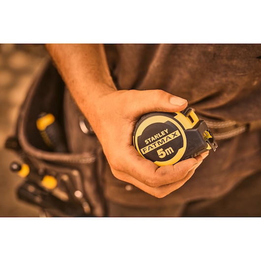 Foto van STANLEY FMHT33100-0 FATMAX 5m rolmaat in hand, gereedschapsriem op de achtergrond.