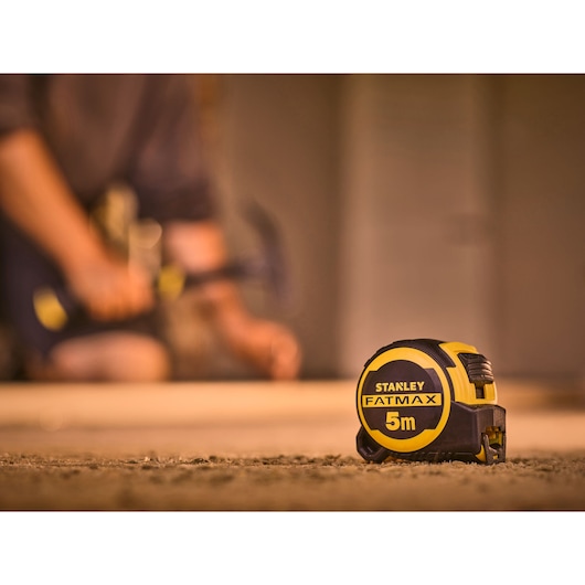 STANLEY FMHT33100-0 FATMAX 5m rolmaat scherp in beeld, bouwomgeving met wazige figuur op de achtergrond.